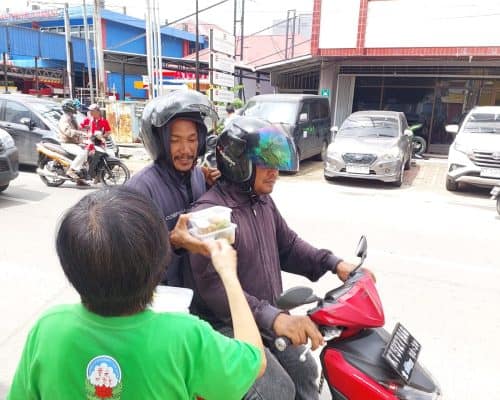 Relawan Lotus Light Charity Society bagikan makanan kepada pengendara motor di jalan kota.