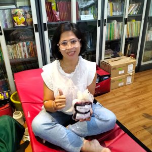 Perempuan tersenyum memegang paket bantuan di ruang perpustakaan.