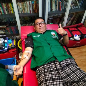 Donor giving blood in donation room with bookshelves in background.