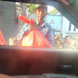 Pengemudi menyerahkan paket bantuan kepada penerima di luar mobil.